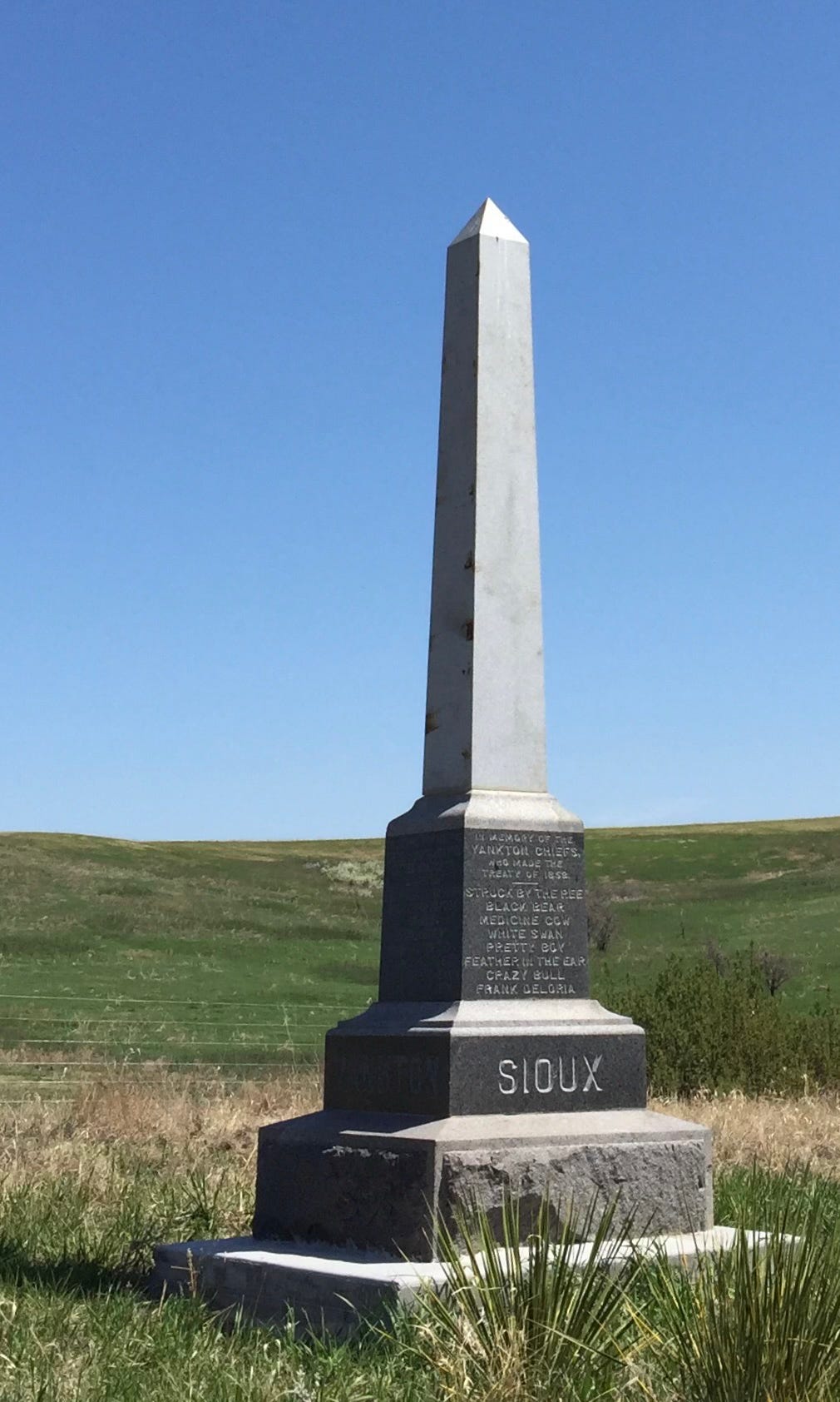 An obelisk set against blue sky, the word Sioux carved into the base, and, in smaller letters, names are carved
