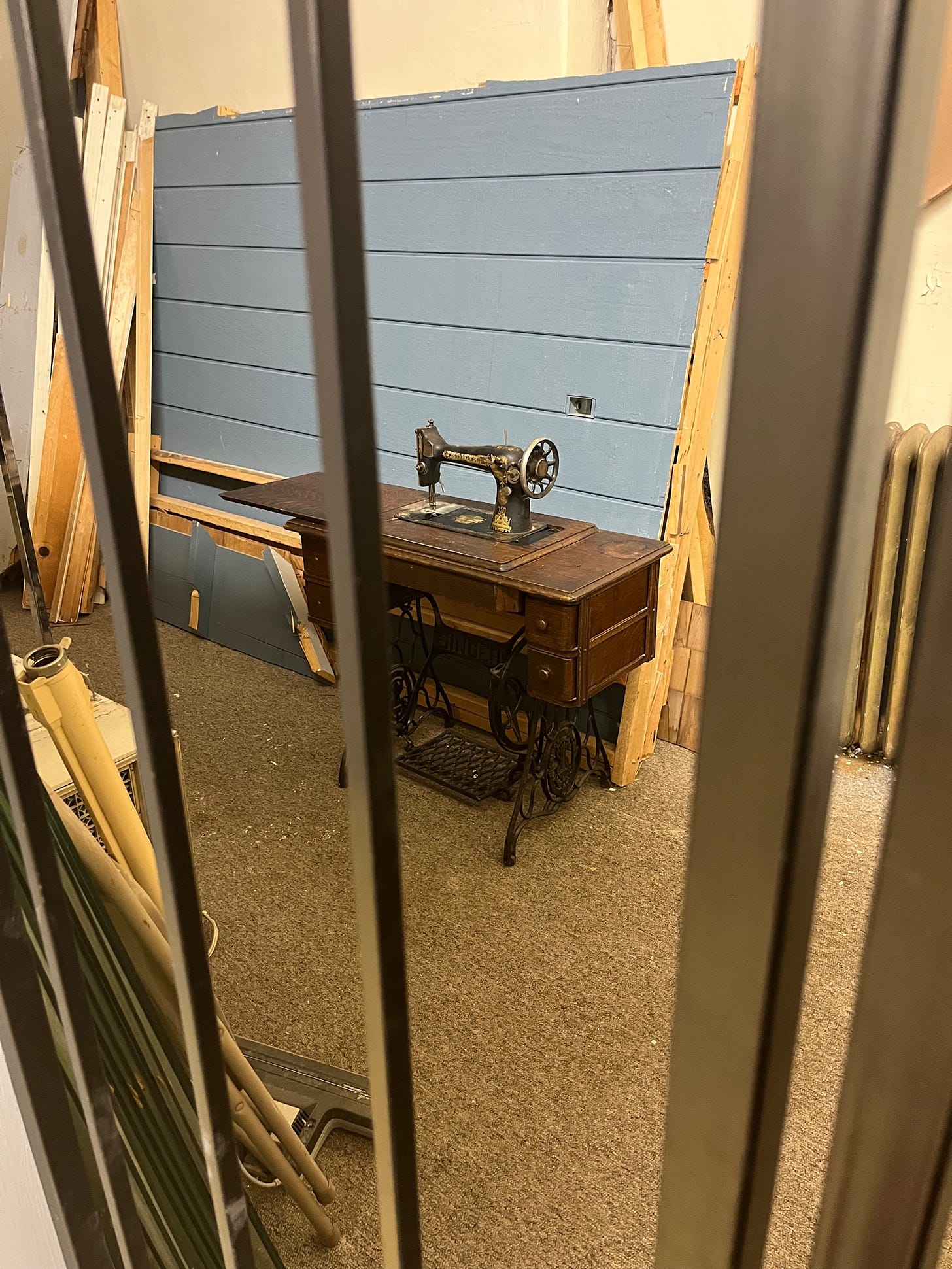 An antique sewing machine and table in an unfinished room behind an iron door