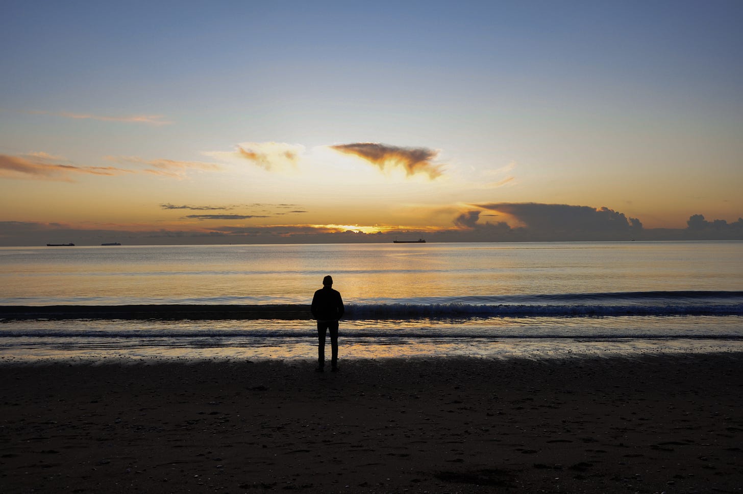 A silhouette of a man looking out across the water, where the sun is just beginning to rise. The sky has a faint tinge of yellow.