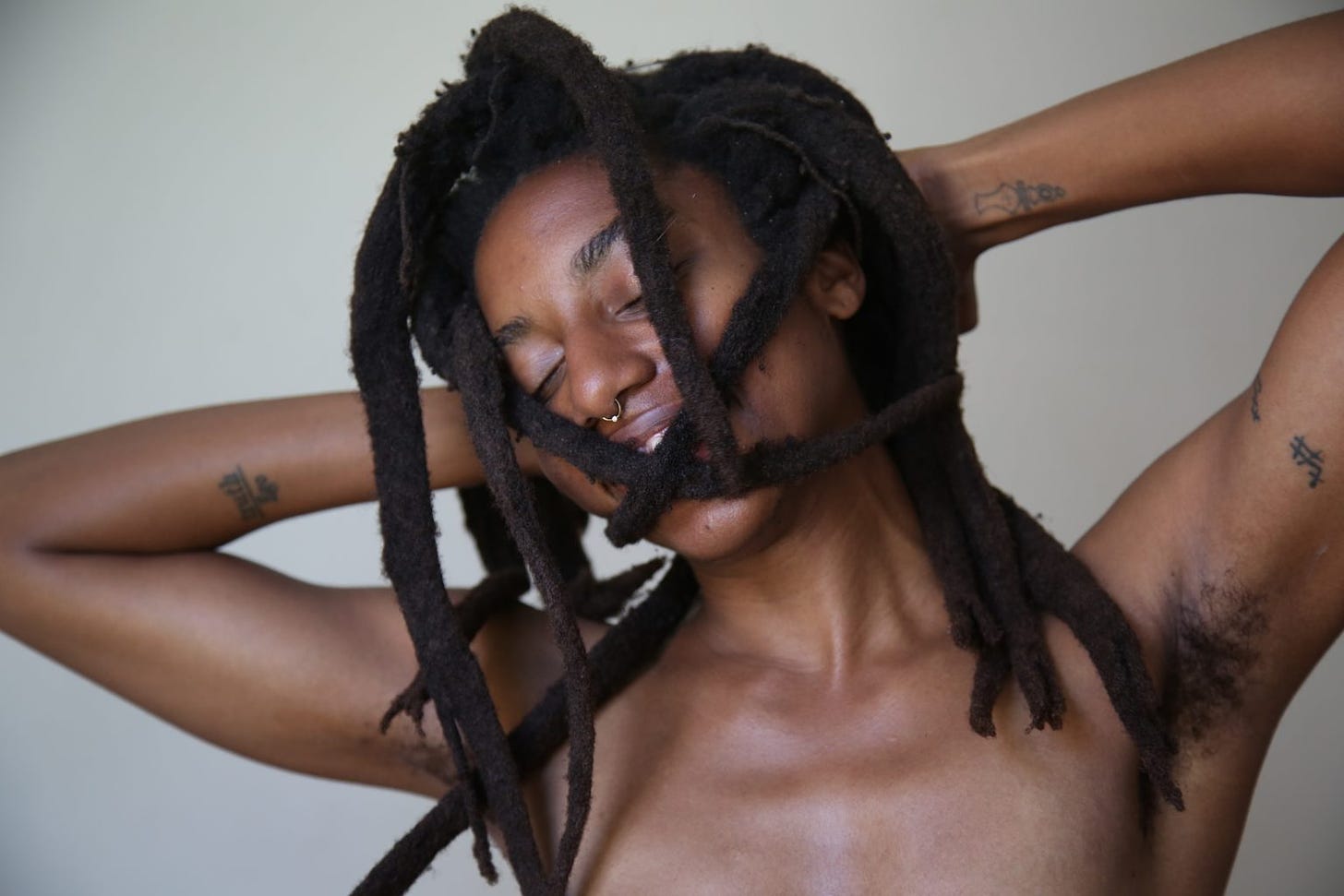 a black woman smiling with her eyes closed while holding two of her dreadlocks in an X shape over her mouth