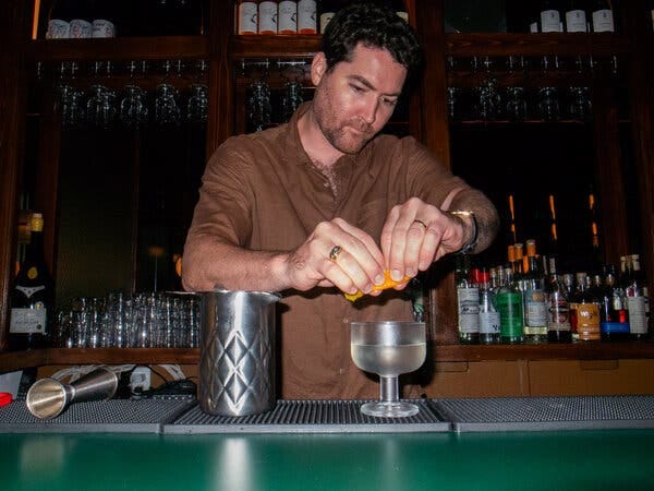 A bartender squeezes orange peel over a cocktail in a squat stem glass.