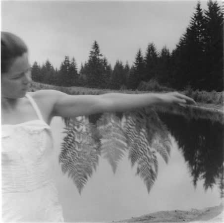 Francesca Woodman’s 1980 image — a woman stands in a tree lined landscape next to a lake, one arm outstretched. Ferns hang from her arm, but it looks like she’s part of a reflection or even becoming part of the forest itself, like Daphne