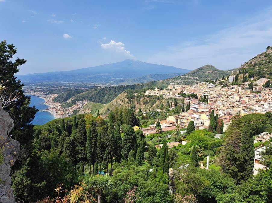 Taormina on a hill with trees and Mount Etna in the background