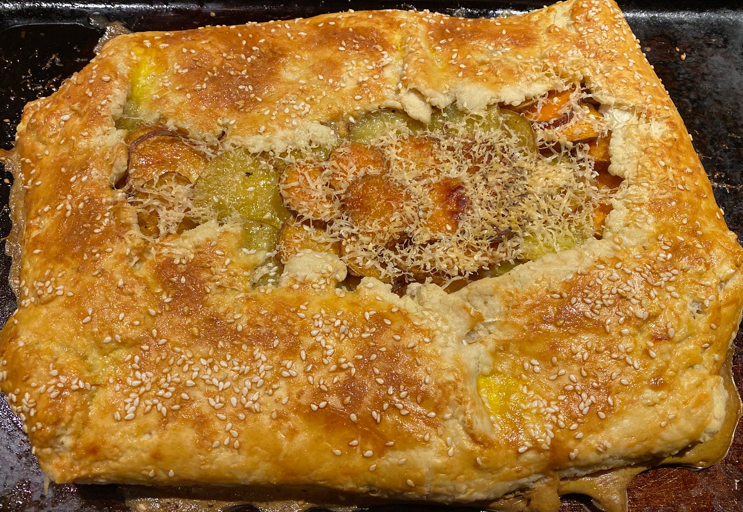 A golden brown rectangular galette sprinkled with sesame seeds; layers of thinly sliced potatoes and sweet potatoes peek out of the middle.