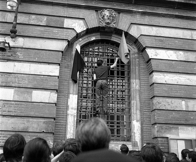 A student hanging an anarchist and communist flag in Toulouse, France in 1968.