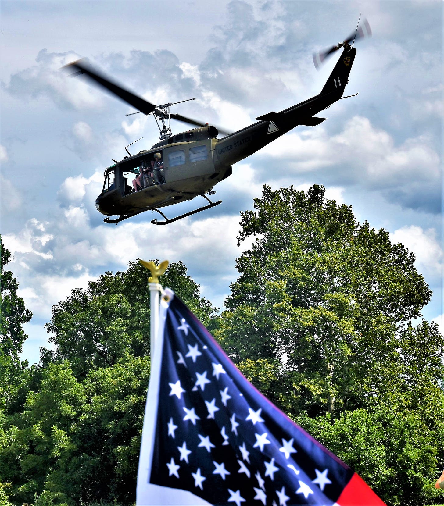 A Huey helicopter flies over an American flag.