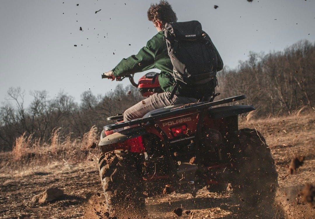 man riding red atv on brown field during daytime man riding red atv on brown field during daytime