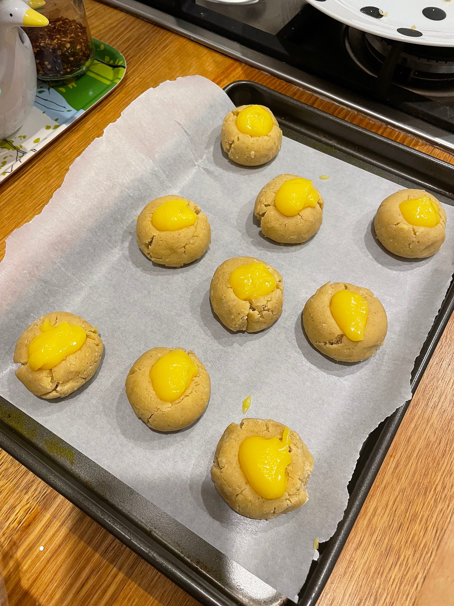Tray of thumbprint cookies with lemon curd in place of jam ready to go into the oven. They sit on a tray with swan measuring cups nearby.