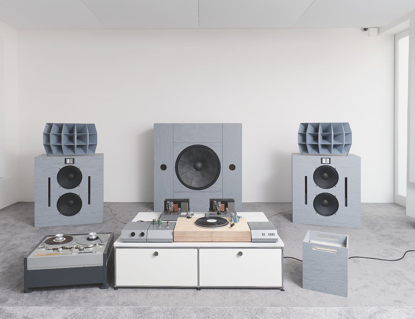 Photograph of a custom-built sound system made with grey materials situated within a white room with grey carpet