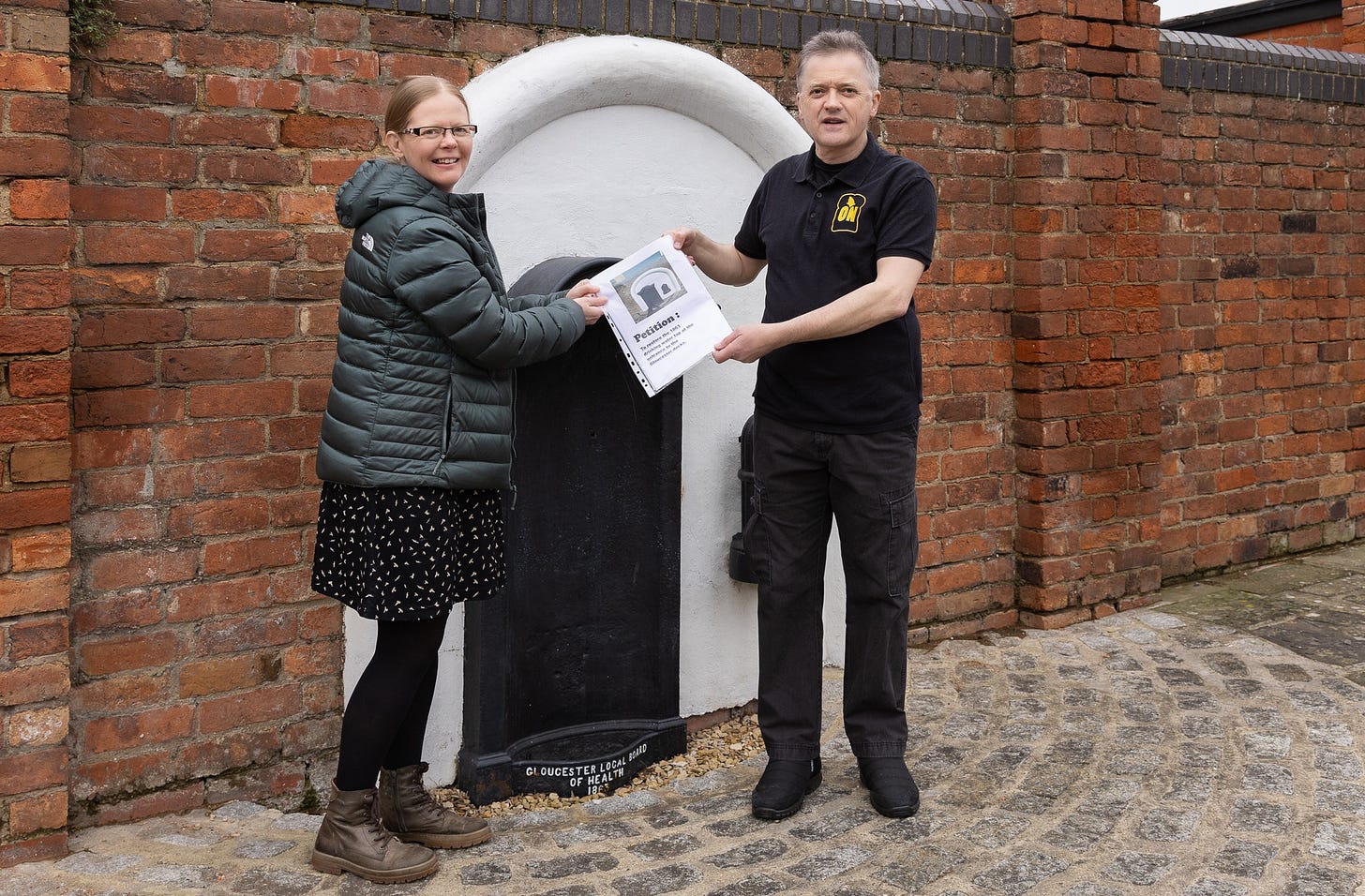 A picture of two people standing in front of a black water tap holding the paper petition together.