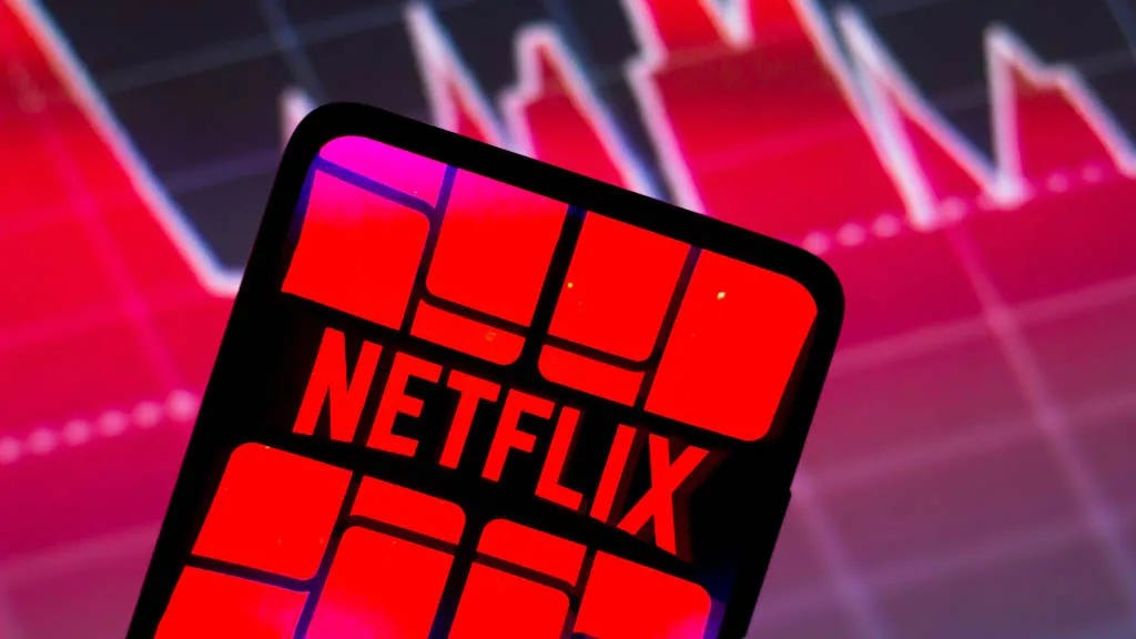 The Netflix logo on a phone in front of a stock market graph