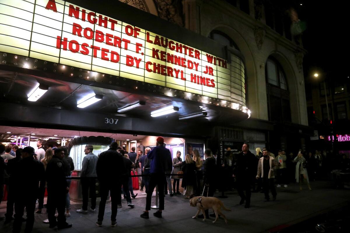People stand outside a theater, its marquee reading "A Night of Laughter With Robert F. Kennedy Jr / Hosted by Cheryl Hines"