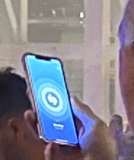 Grainy zoomed in picture of a white man holding up his phone with Shazam on the screen