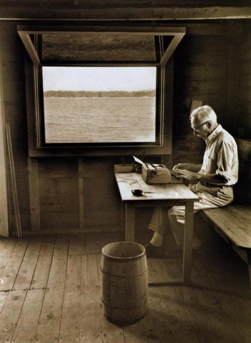 A man typing on a typewriter beside the window with a view of the lake