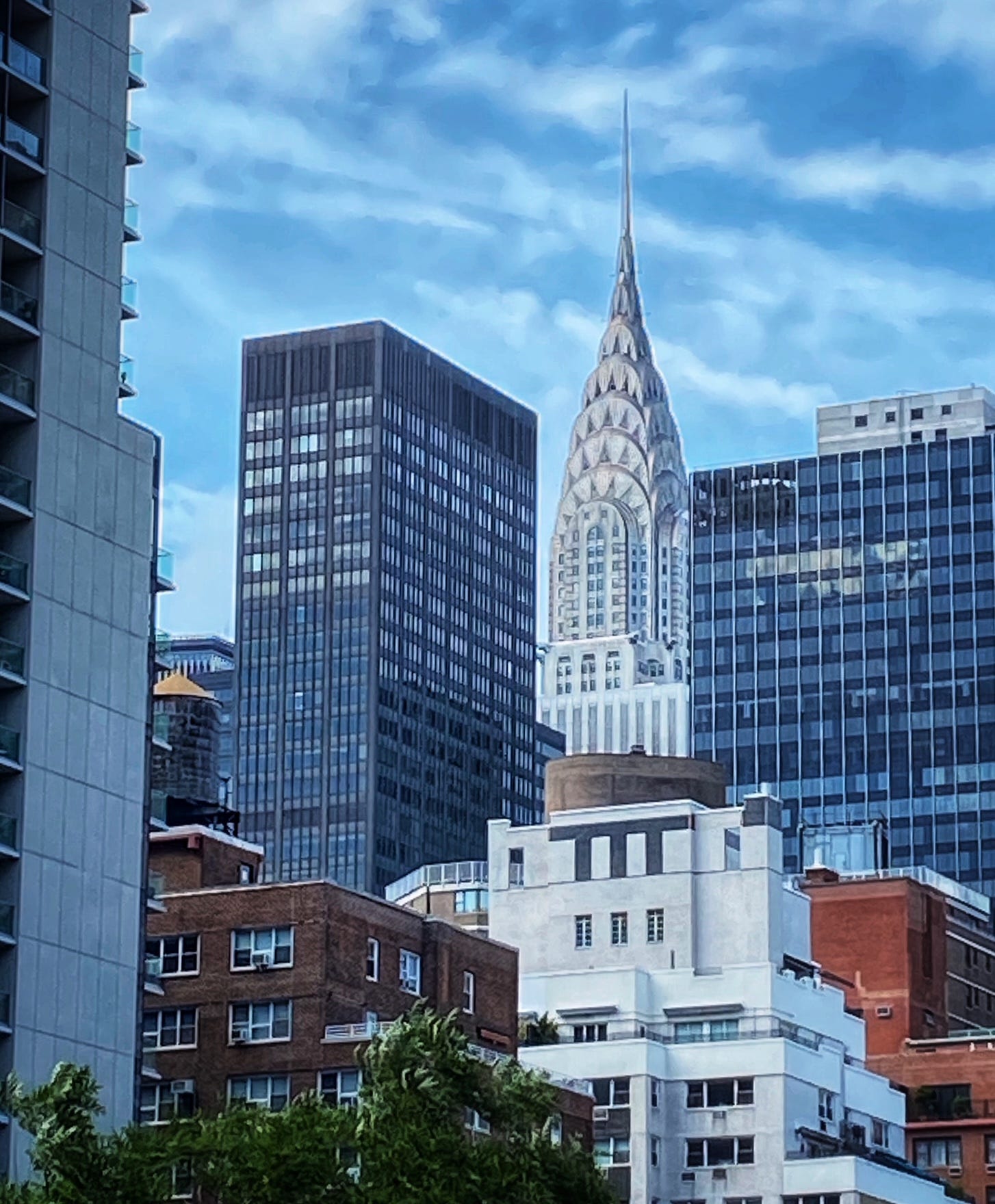 A water tower is visible on a roof between taller buildings. Also visible in the gap between office buildings is the Chrysler Building.