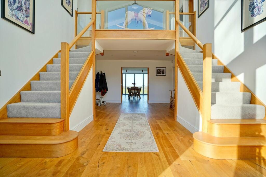 A staircase that comes down on both sides in a large hallway. The bottom two steps aren't carpeted which feels dange.
