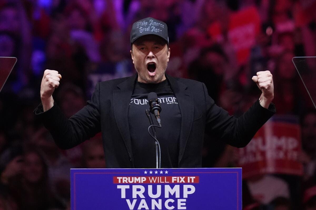 Elon Musk wearing a cap and shouting into a microphone at a podium with a Trump-Vance sign 