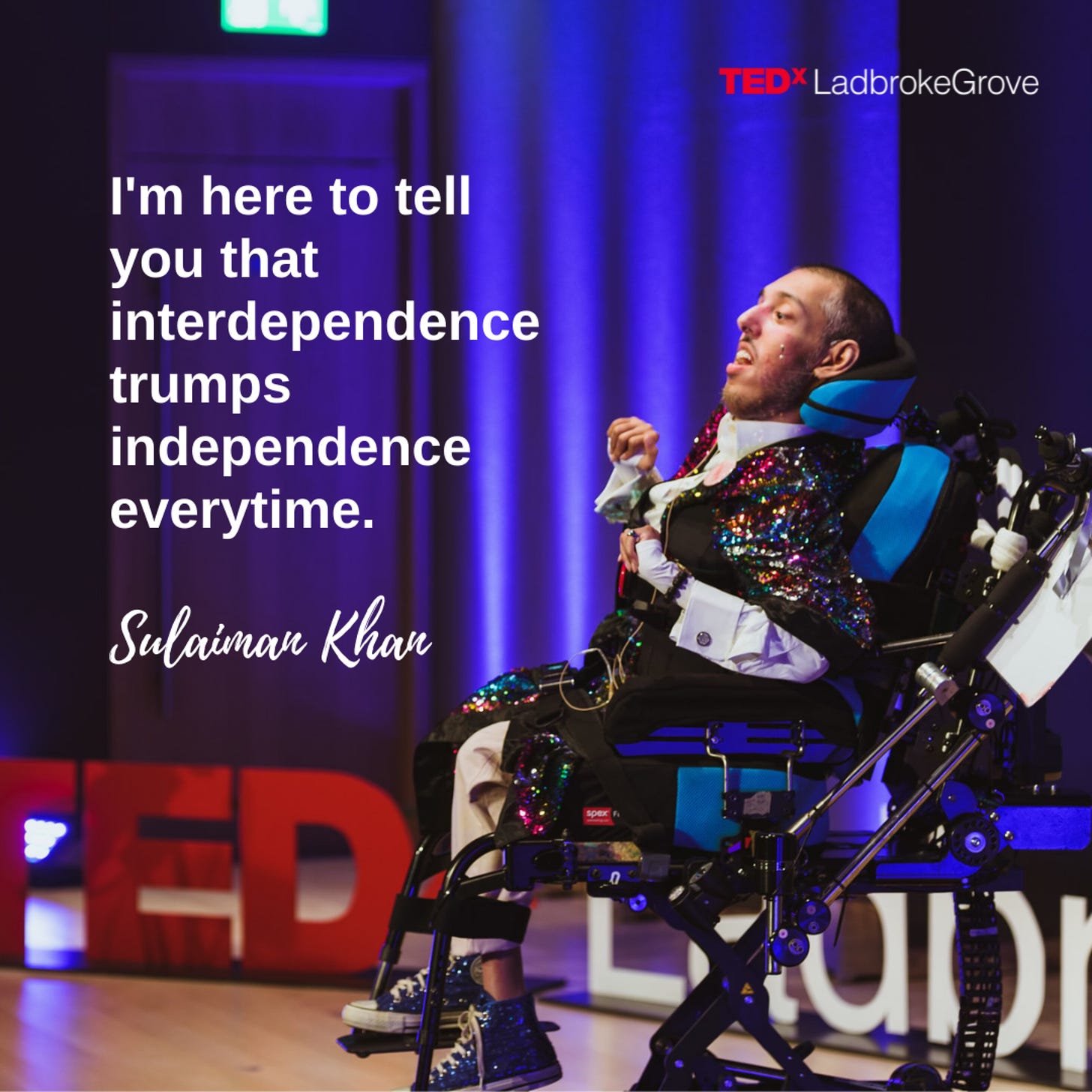 IMAGE 1 DESCRIPTION: A vertical graphic showing a left side view photo of Sulaiman (sitting in his power wheelchair) on the TEDxLadbroke Grove stage giving his first TEDx speech with an ear microphone on his left ear. The stage has pale tan wood flooring with a purple curtain and dark purple wall. There is a structure on the stage of the words, “TEDxLadbrokeGrove.” The ‘TEDx’ is red and the rest is white. Sulaiman is a wholehearted Disabled and South Asian man who is positioned in front of the words structure and to the right half of the picture. He is wearing a long sleeved white french cuff dress shirt with cufflinks and a multi-coloured sequined short sleeved kimono on top. He also has on a pair of blue sequined converse shoes and pink chino trousers. Above him are the words, “TEDxLadbrokeGrove” with TEDx in red and the rest in white text. To the left of him is white text that says, “I’m here to tell you that interdependence trumps independence everytime.” Below that text is cursive white text saying, “Sulaiman Khan.”