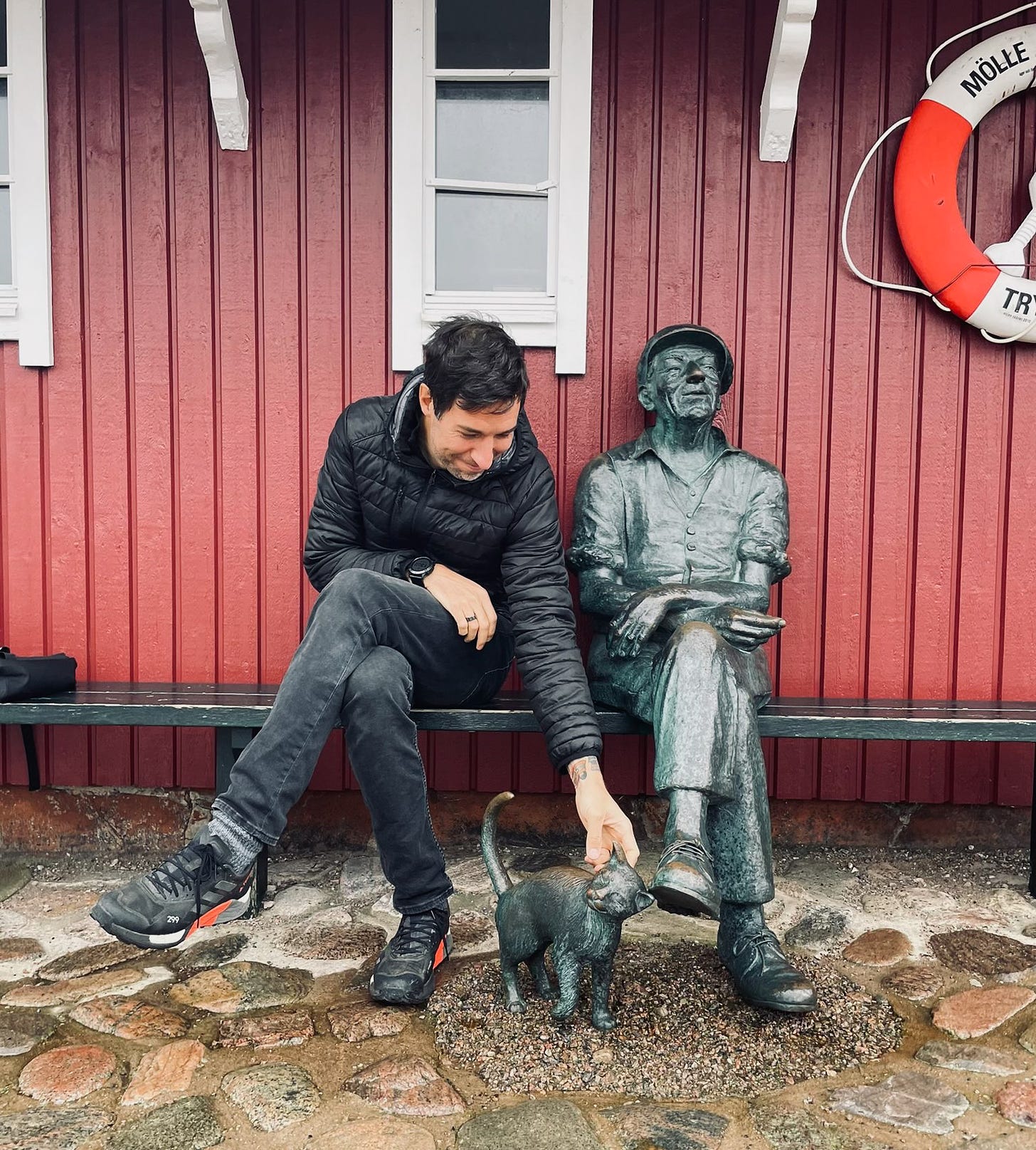 Der Autor auf einer Bank mit einer Statue von einem schlafenden Mann und einer Katze in Mölle, Schweden