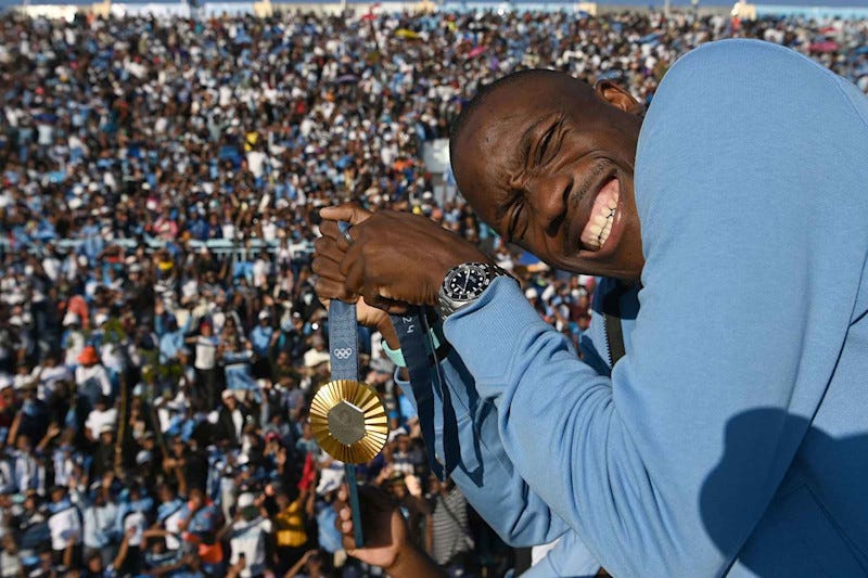 Olympic gold medallist, Botswana's Letsile Tebogo, who won the men's 200m athletics event during the Paris 2024 Olympic Games, holds his gold medal as he arrives on an open bus at the Botswana national Stadium during a welcoming ceremony in Gaborone on 13 August 2024. Botswana gave a rapturous welcome to Letsile Tebogo on Tuesday as the sprinter returned home with the southern African country's first ever Olympic gold medal. Families with children, elderly people and young supporters waved Botswana's sky blue, white and black national flag as the Olympic team landed back in the capital Gaborone. Hundreds of supporters had gathered at the small airport, benefiting from an impromptu half-day holiday declared by President Mokgweetsi Masisi to celebrate Tebogo's success. (Photo by Monirul Bhuiyan / AFP) (Photo by MONIRUL BHUIYAN/AFP via Getty Images)