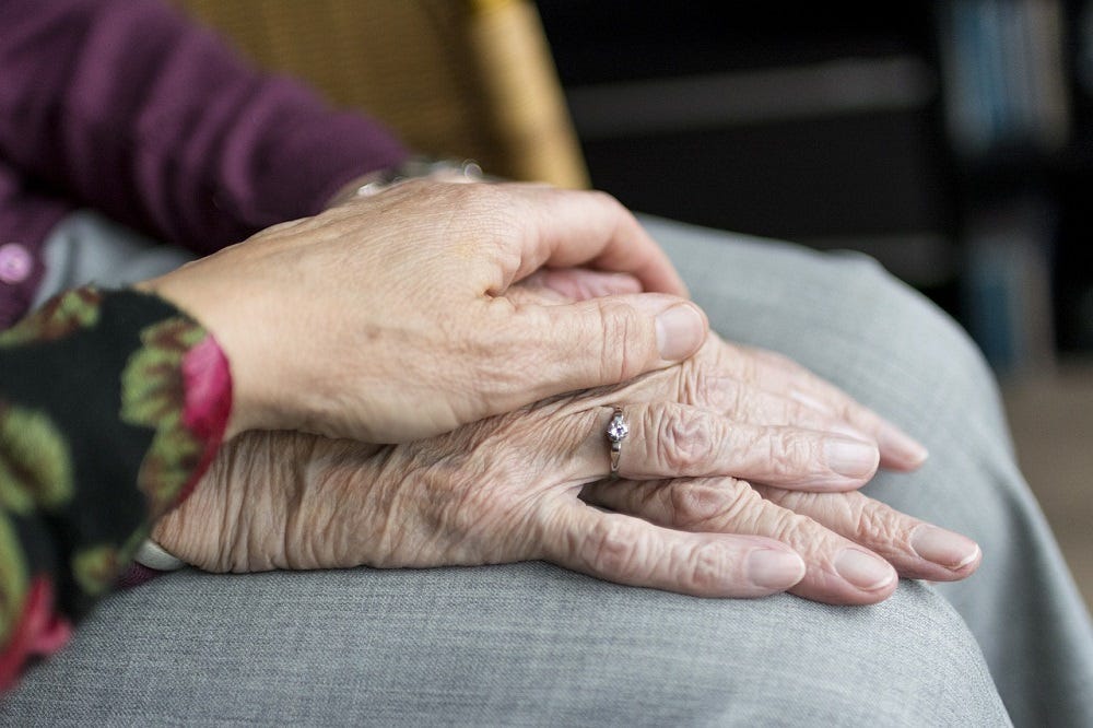 A daughter holds the hand of her elderly mother in close up.