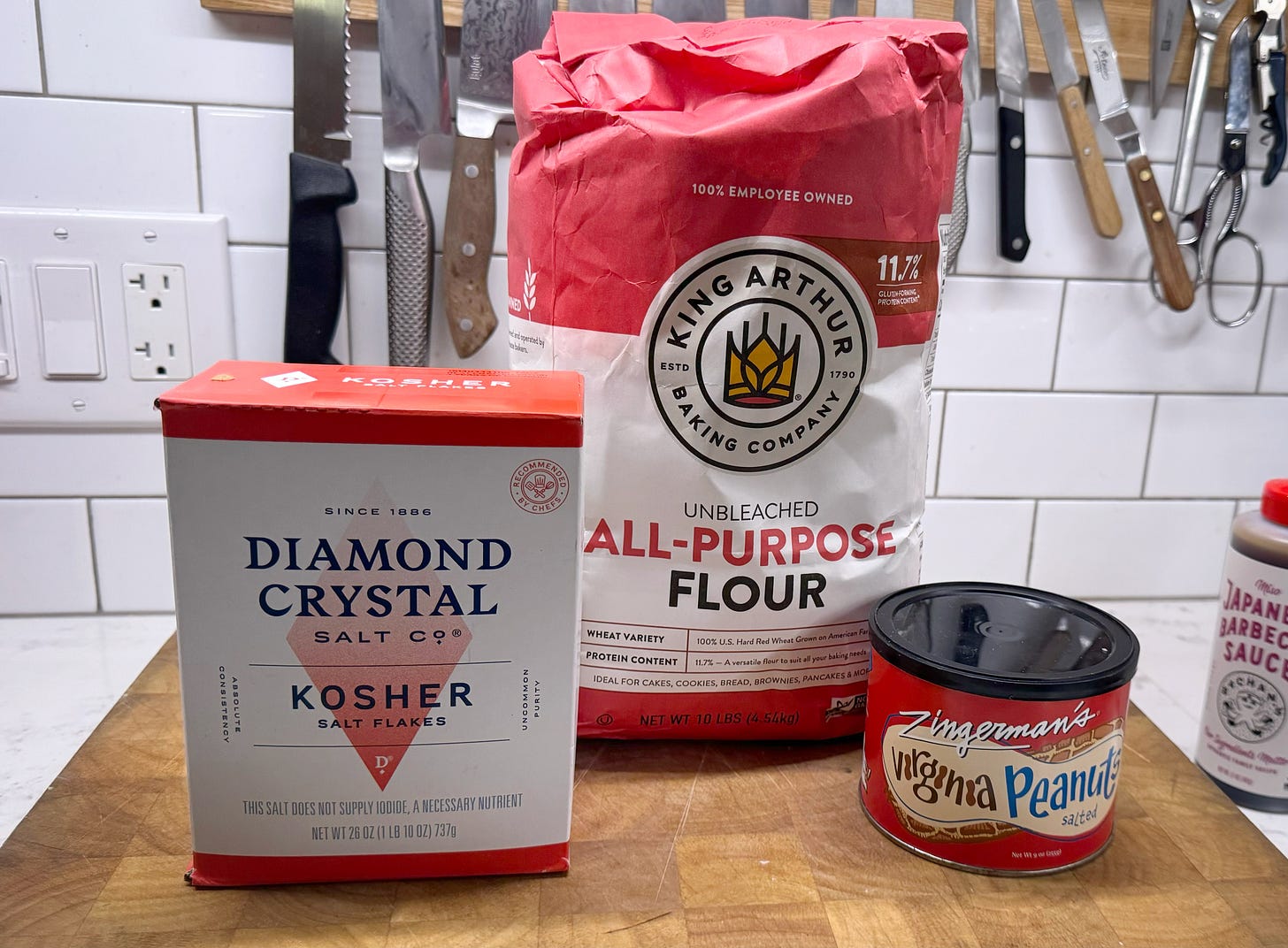 A photo, from left to right, of a box of Diamond Crystal Salt Co. Kosher Salt Flakes, a 10-lb bag of King Arthur All-Purpose Flour, and a tin of Zingerman's Salted Virginia Peanuts