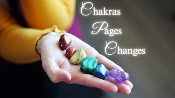 A hand outstretched holds seven stones in rainbow hues: Chakras, Pages, Changes.