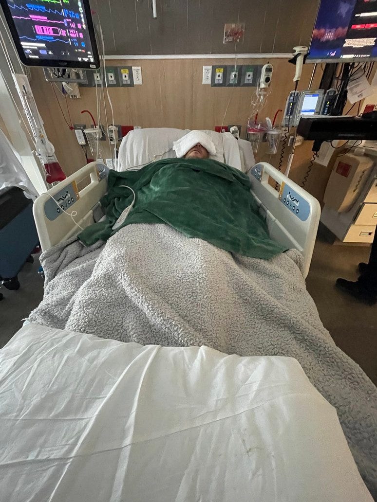 a man lies in an ICU bed with wires monitoring him. There's a green blanket over him. a man lies in an ICU bed with wires monitoring him. There's a green blanket over him.