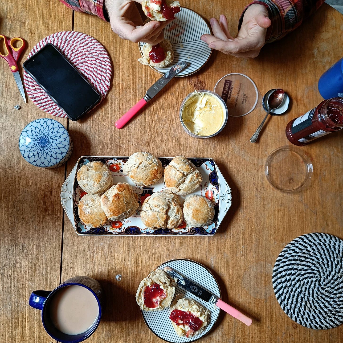 Photo taken from above of scones, clotted cream, jam, cups of tea, plates, and James' hands. Photo taken from above of scones, clotted cream, jam, cups of tea, plates, and James' hands.