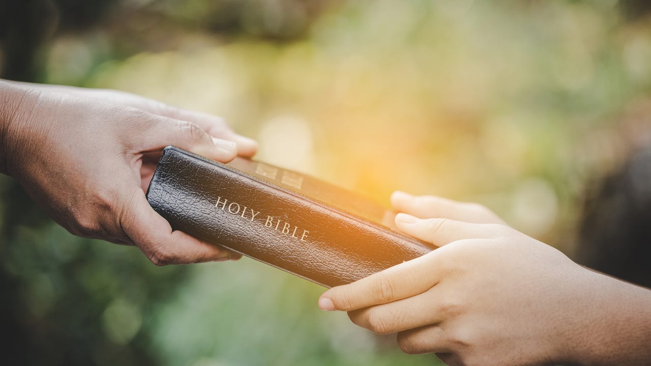 A person handing a Bible to another person.