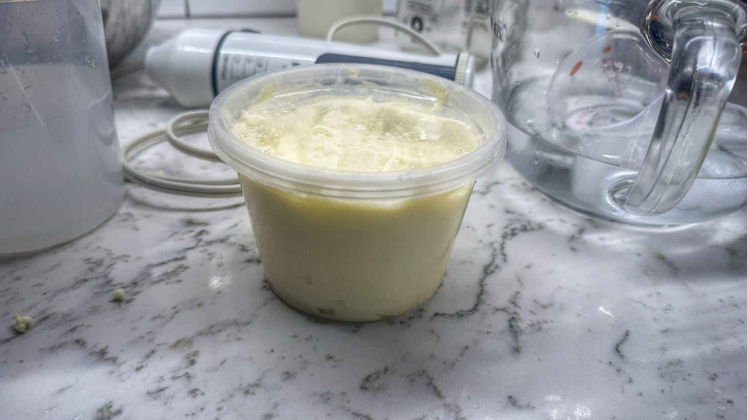 The end result: a 500 ml deli container filled almost completely with butter. Beside it is the remaining ice water from the washing. Behind it is the immersion blender. 