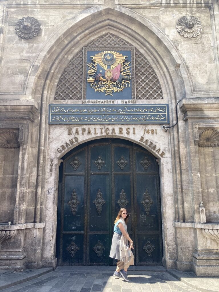 Stone archway entrance to the Grand Bazaar with golden coat of arms under the arch.