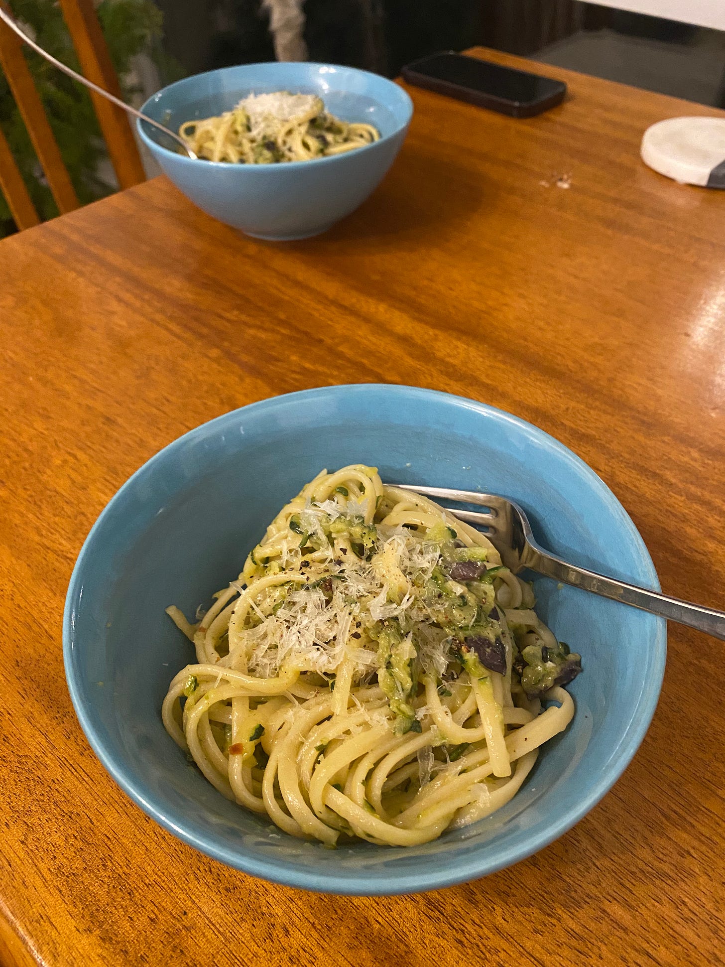 Two blue bowls of linguine with a creamy shredded zucchini sauce, and parmesan sprinkled on top.