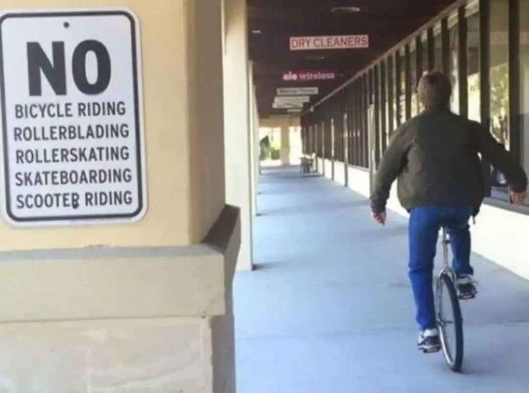 Person unicycling past a sign that says "NO bicycle riding, rollerblading, rollerskating, skateboarding, scooter riding."