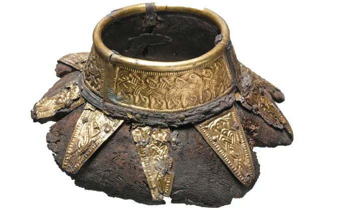 The remains of a wooden drinking vessel with filigree-decorated bronze fittings around the rim, with triangular fittings radiating from the rim.