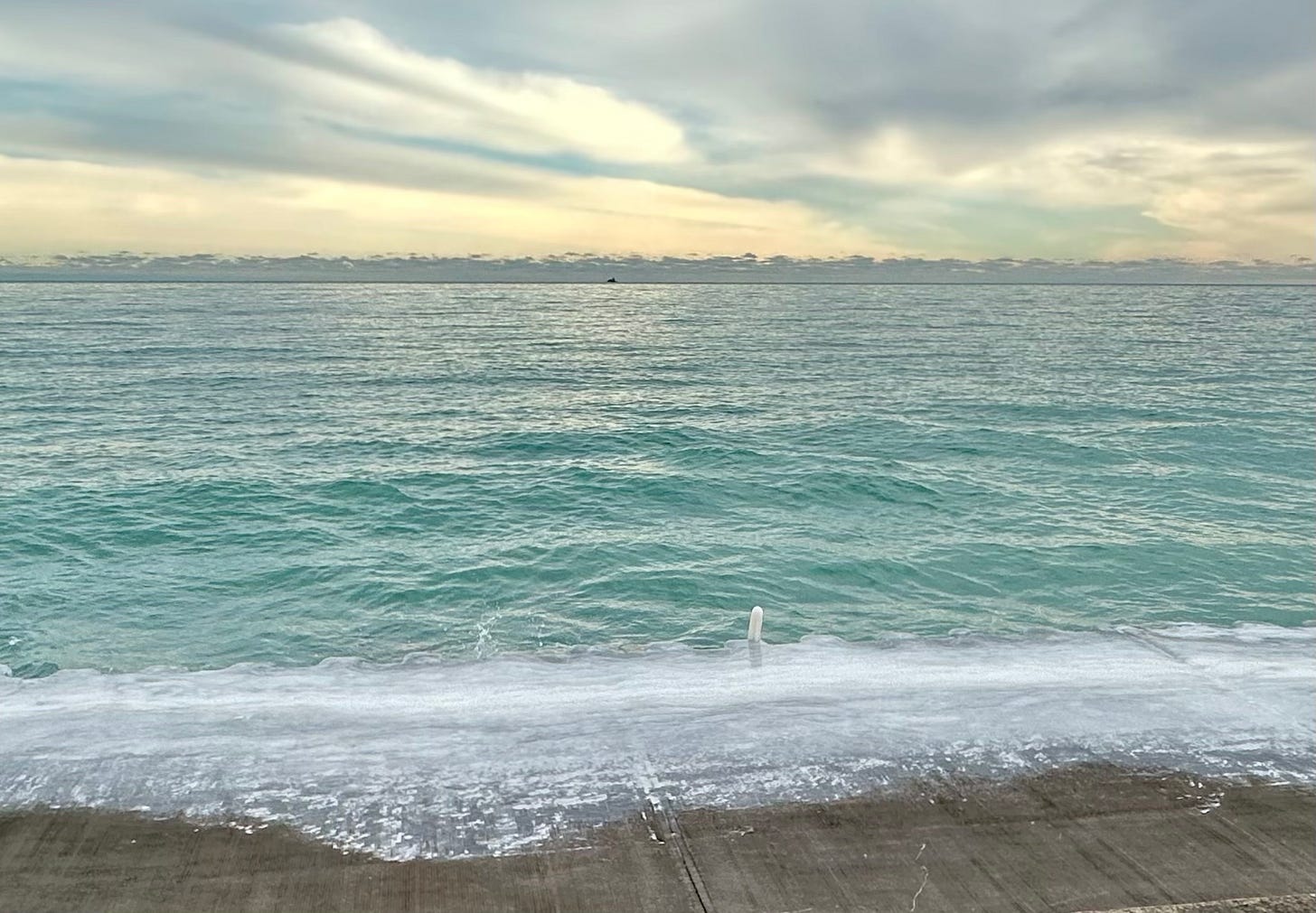 A broad view of a pale green lake Michigan reaching all the way to a horizon of layered clouds and a tiny water crib in the distance A broad view of a pale green lake Michigan reaching all the way to a horizon of layered clouds and a tiny water crib in the distance