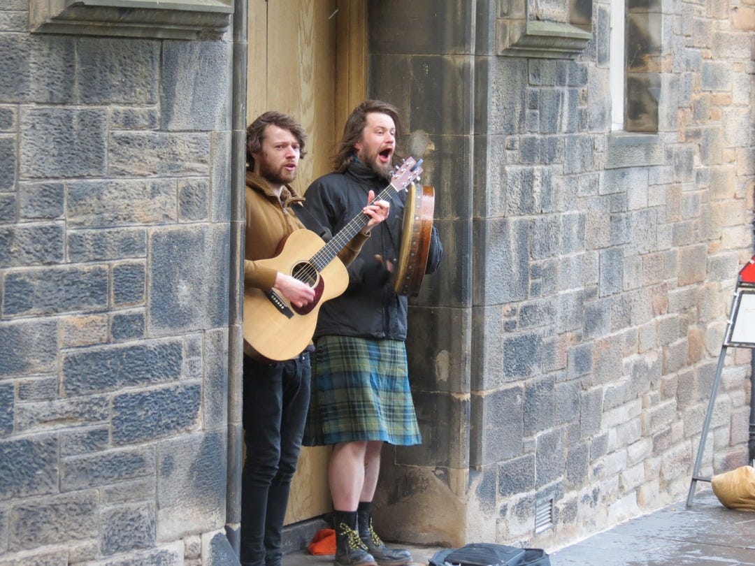 Two men in kilts singing and playing guitar outside a pub in Eninburgh