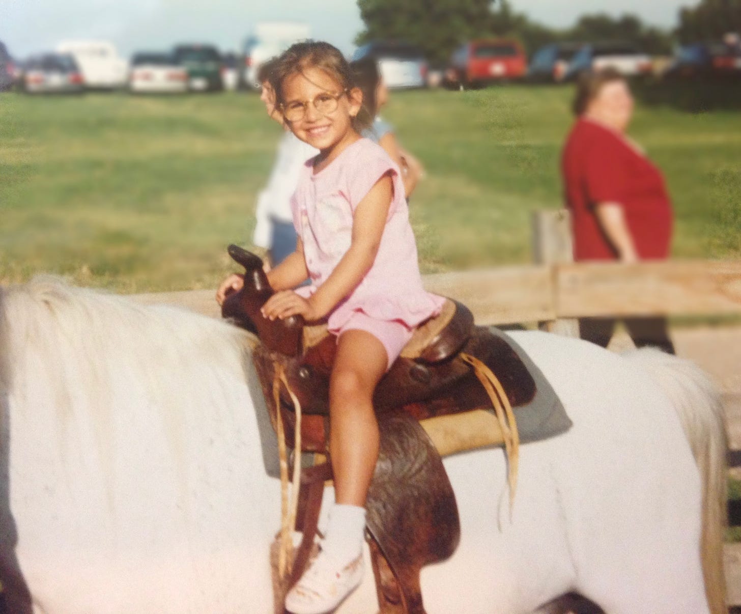Little Shohreh is pictured in matching baby pink shorts and a top sitting on a brown saddle atop a white horse.