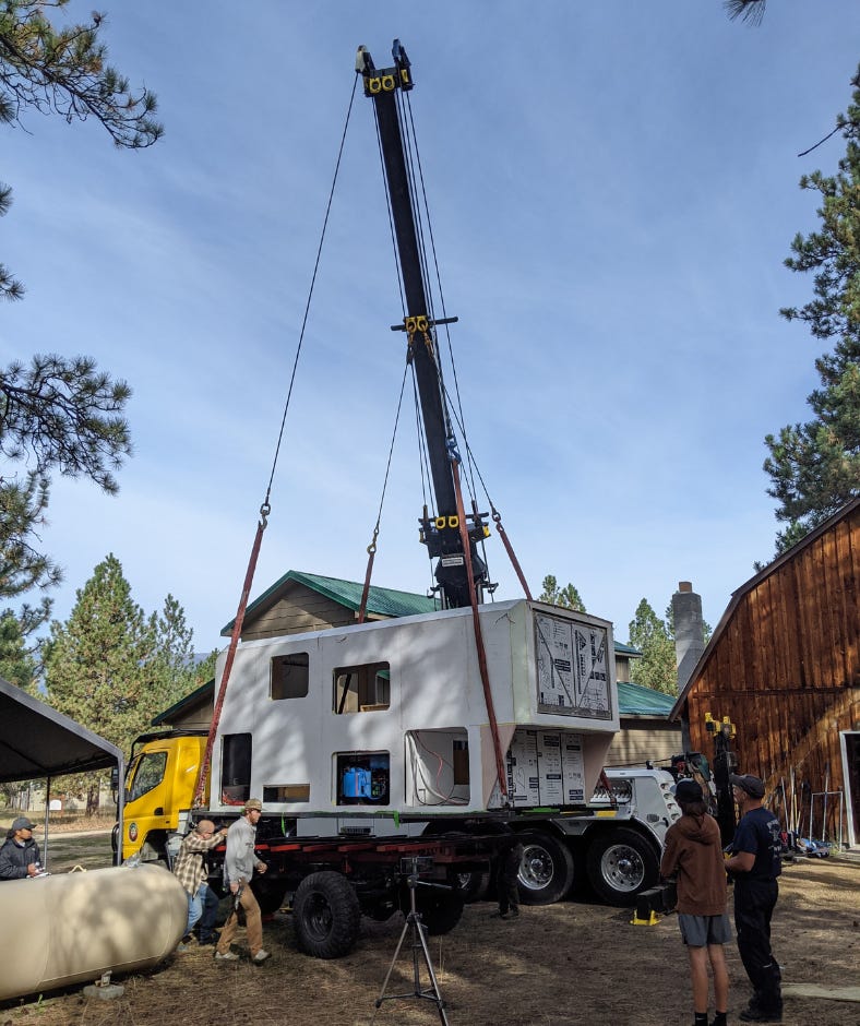 a large crane lifts the box and carries it to the truck, parked nearby