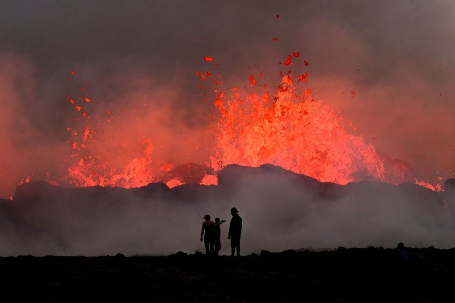 Two people watch lava erupt and flow during a volcanic eruption.