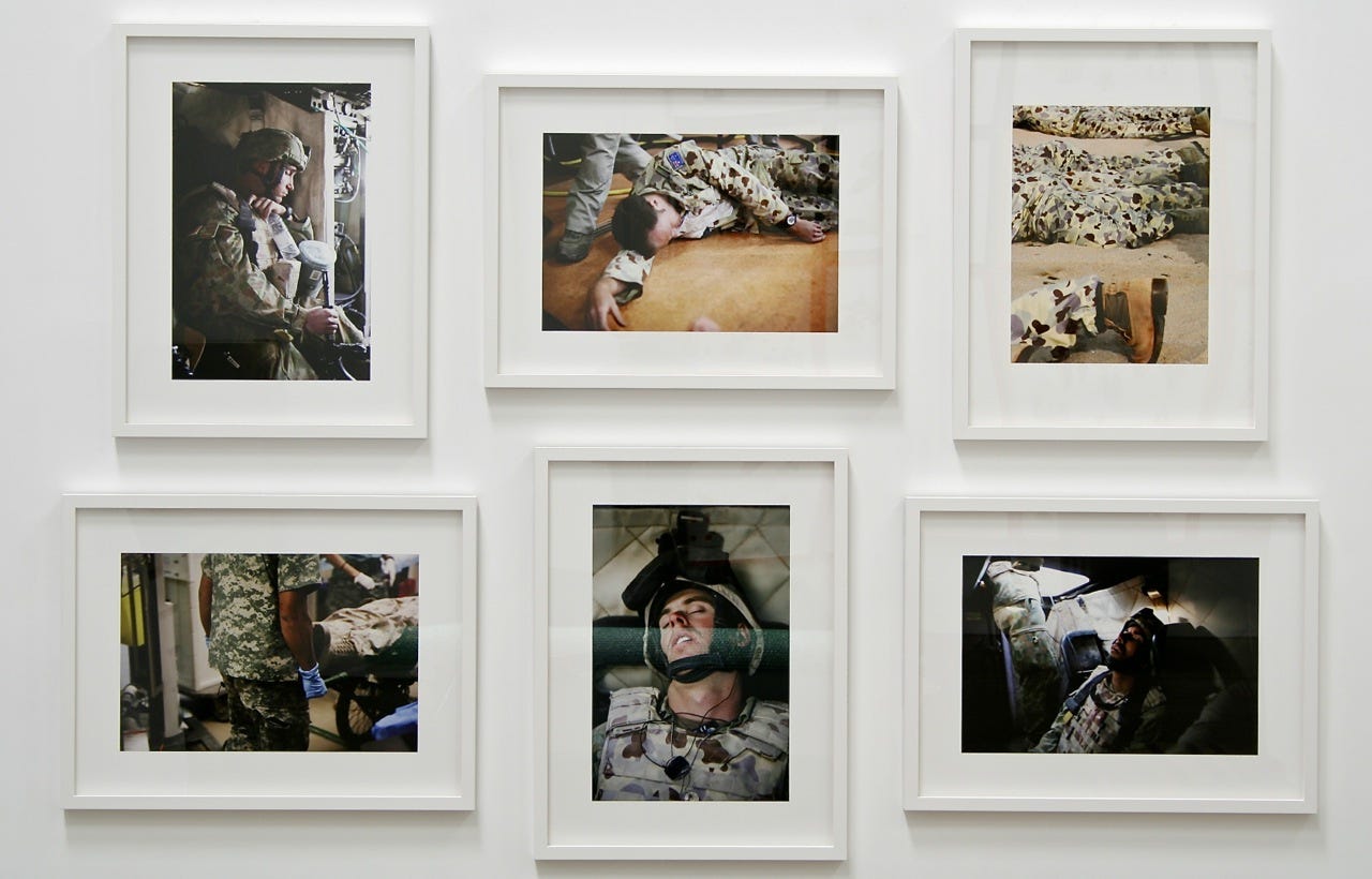 Six photographs of Australian soldiers sleeping in various settings are framed and hanging as a collection on a gallery wall.
