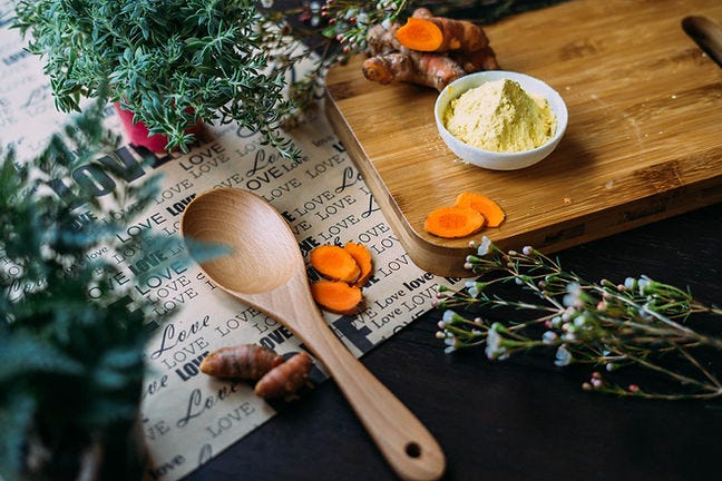 Picture of cutting board, wooden spoon, spices, flowers and herbs, with a page that has the word 'love' written over it.