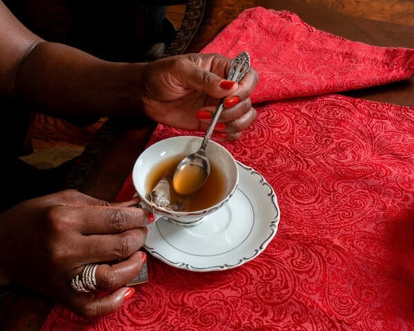 A person uses a spoon to stir a cup of tea in a china cup. The tea bag is still in the cup.
