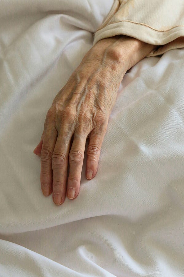 an elderly person’s hand, lying on the bed.