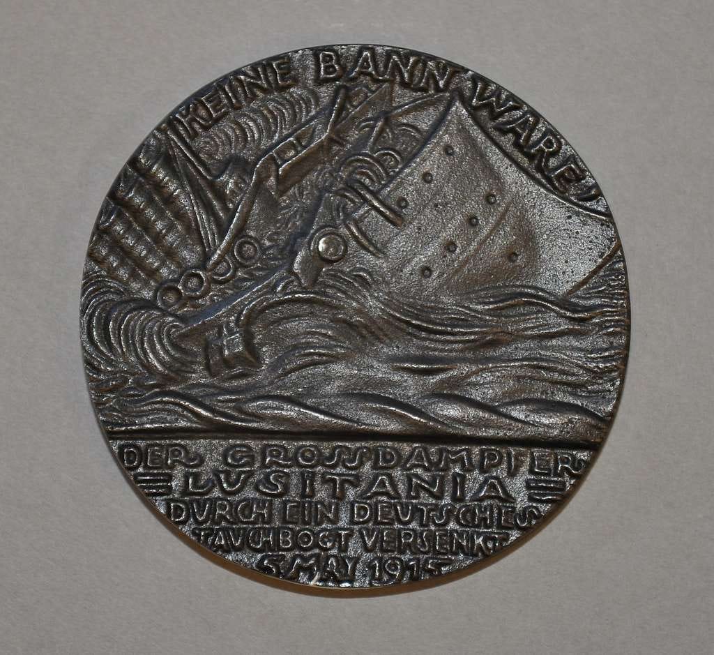 A photo of a commemorative medal struck to mark the sinking of the Lusitania. The medal shows the ship sinking into a tumultuous sea. There is a German inscription along the bottom of the medal, which proclaims the sinking and the date.