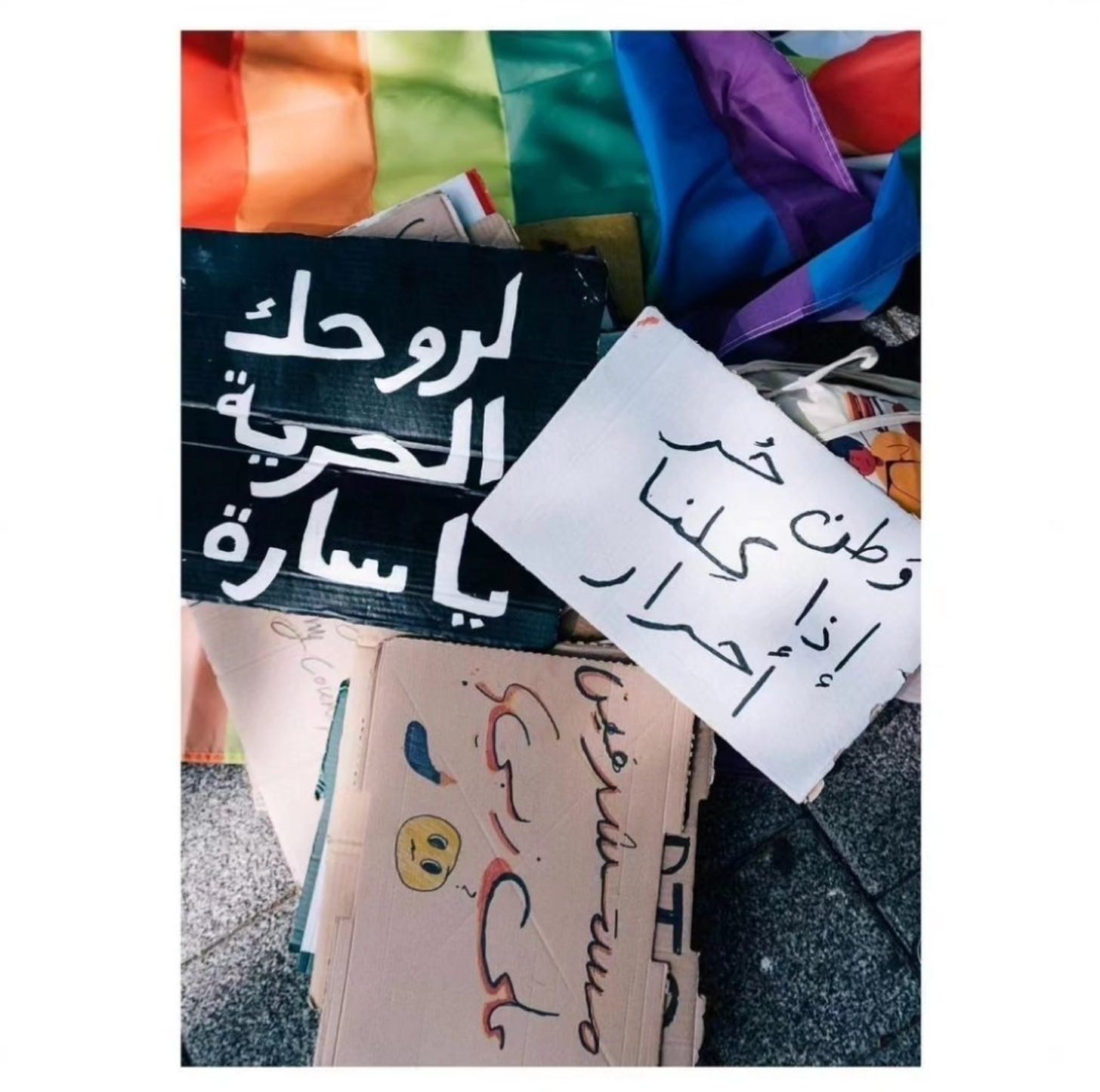 a pile of cardboard signs with Arabic characters lying on the street on top of a rainbow Pride flag