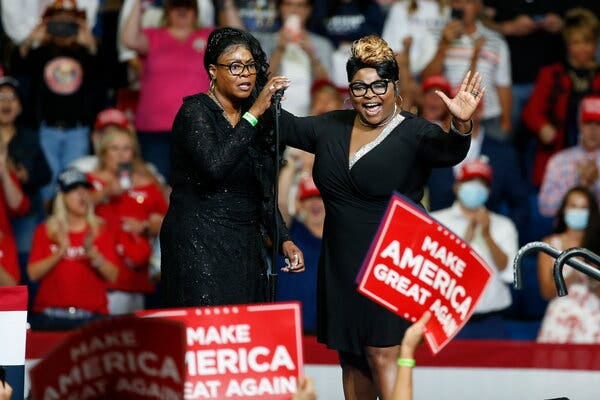 Lynette Hardaway and her sister, Rochelle Richardson, the pair known as Diamond and Silk, speaking onstage during a campaign rally for Donald Trump. Some in the audience raise signs that read “Make America Great Again.”
