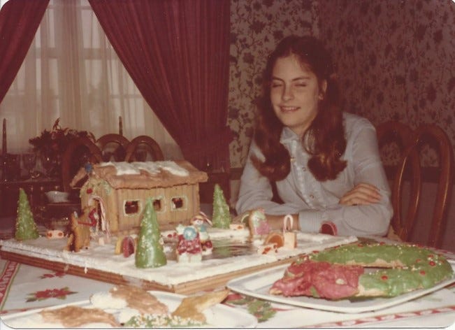 Teen girl sits proudly by the gingerbread house and village she created all by herself