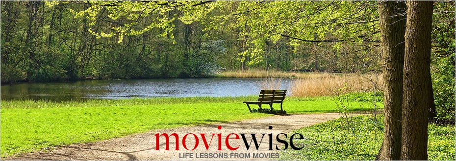A welcoming empty wooden bench facing a pond is situated near a gravel footpath surrounded by a lush green lawn. 