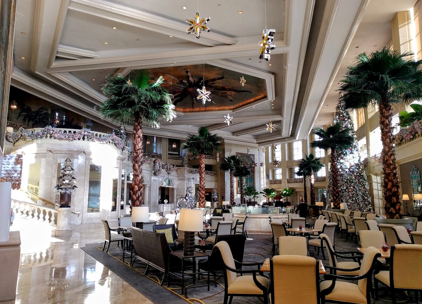 Palm trees, a large, fake Christmas tree, and other Christmas decorations stand in an elegant hotel lobby